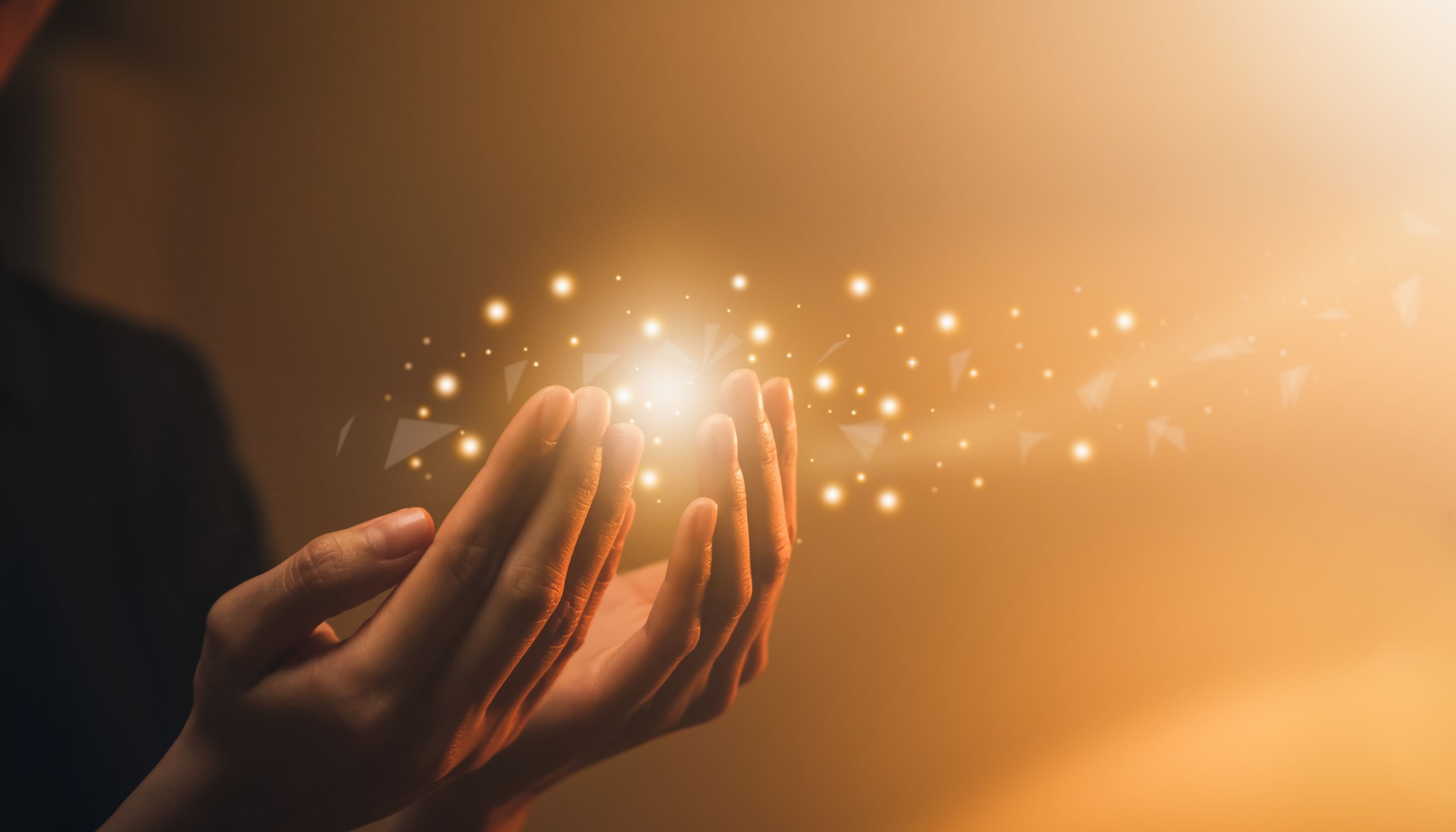 Hand praying with magic light that flows through on orange bokeh background.